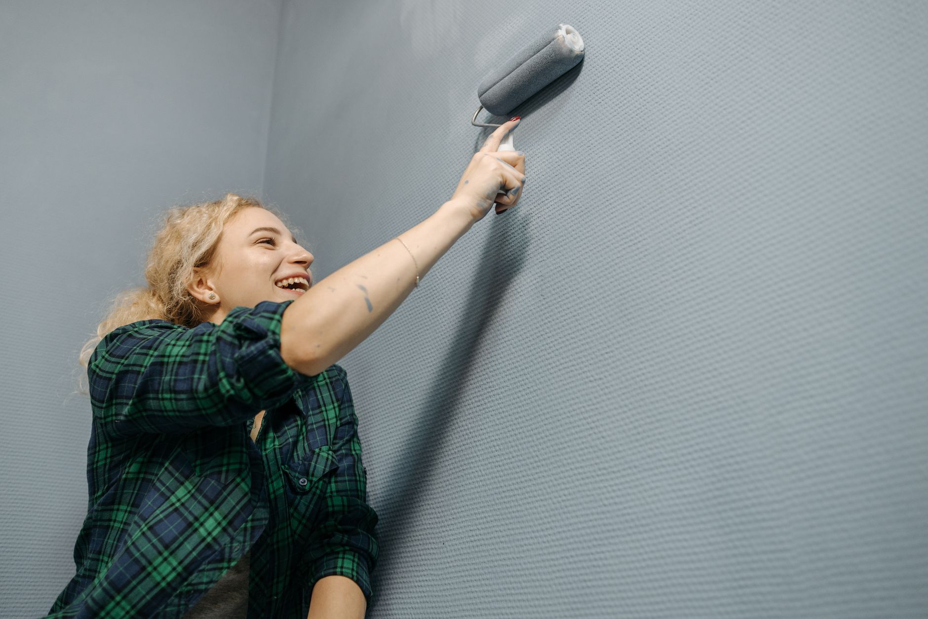 Laughing woman painting a blue wall indoors with a roller brush during home renovation in Santa Monica, CA